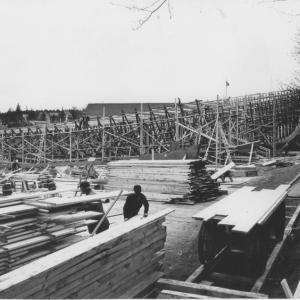 This 1953 East Boothbay view looks south to the Hodgdon yard building. The Lincoln Street yards are out of sight on the right. Four future minesweepers are shown, two with their tall stems in place on the far right, and two with their keels laid only. The men are working on extending the planking over the mudflats and on the scaffolding next to one of the skeletal ships. In the right foreground is the track and the handcar with short lengths of planking on top. Courtesy of Robert Rice