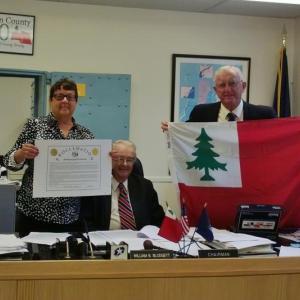 Lincoln County Commissioner Mary Trescot holds the proclamation issued by Lincoln County to commemorate Monhegan Island’s 400th anniversary. Commissioner Hamilton Meserve raises the Lincoln County flag as Commissioner William Blodgett looks on. JANE CARPENTER/Wiscasset Newspaper