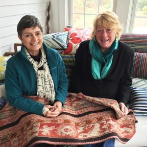 Kathleen Jones, left, and Diana Kerr of Kerr/Jones Design in Kerr’s sunroom in East Boothbay surrounded by their pillows, and holding a manta from Peru. SUZI THAYER/Boothbay Register