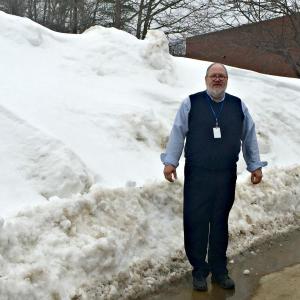 Boothbay Region Elementary School Principal Mark Tess stands outside where the entrance to the playground should be, where a snowbank taller than he is stands instead. KATRINA CLARK/Boothbay Register