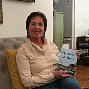 Author Cheryl Blaydon in her East Boothbay home, holds a copy of her newest novel “The Heart of Stone.” KATRINA CLARK/Boothbay Register