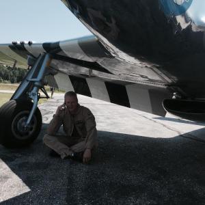 Texas Flying Legends Museum pilot Mark Murphy takes a phone call under the wing of a World War II, P-51 Mustang shortly after landing it at Wiscasset Municipal Airport on July 28. SUSAN JOHNS/Wiscasset Newspaper Texas Flying Legends, Mark Murphy