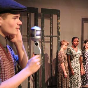Jonah Daiute as a 1920's radio announcer, with factory workers played by, from left, Rachel Schuster, Toru Fiberesima and Noelle Timberlake standing by in a scene from “These Shining Lives.” Courtesy of Heartwood