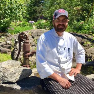 Chef Kelly Patrick Farrin outside his Carriage House Restaurant in East Boothbay. He’s sitting on a stone birdbath made by his father, Pat Farrin. SUZI THAYER/Boothbay Register