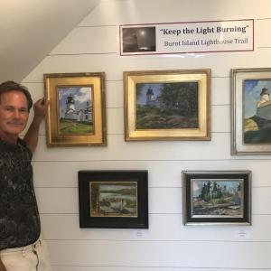 Artist Brad Betts stands near a display of the paintings donated to the Burnt Island benefit auction. Courtesy of Howard Wright