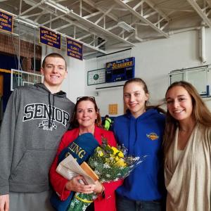 Eileen King, flanked by three Boothbay Region High School seniors, Nick Simpson, Page Brown and Sydney Meader, holds some gifts bestowed upon her during a brief school assembly held in her honor on Wednesday, Dec. 20. King, who has served 24 years in the school system as Boothbay Region Elementary School principal and Superintendent of Schools and is now moving on to another job, was given some flowers and a pullover with the number 24 (her years here) with her name and “Seahawk for Life” sewn on the sleeve. She was also presented with a plaque made from the old gym bleachers that was given by Larry Brown and presented by the three students. Brown wrote up a very nice speech for Eileen, according to BRHS Athletic Director Allan Crocker. King’s last day is Dec. 31 and she will then become the new executive director of the Maine State Superintendents Association. Courtesy of Dick Morrison