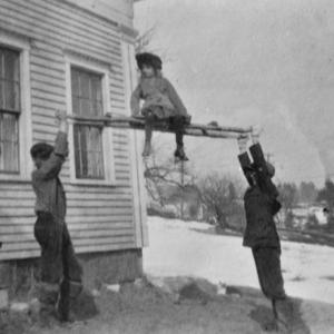 Virginia Frey (Huskins) hoisted on sticks by brothers Bert and Park near the house on Western Avenue at West Harbor. The view looks back to the head of Mill Cove. Courtesy of Jean Huskins Chenoweth