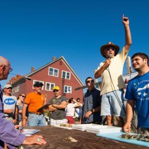 Maine Champion Oyster Shucking Contest emcee Larry Sidelinger (standing center) calls the action as two contestants await the start of their heat at a past Pemaquid Oyster Festival, scheduled this year for Sunday, Sept. 30 at Schooner Landing in Damariscotta. Supervising the activity (left) is David Seybold, the “Grand Kahuna” of the Maine Champion Oyster Shucking Contest. Courtesy of scottbsmith.com