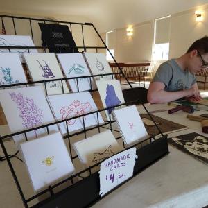 Jaime Wing, hard at work carving a new block, displays his greeting cards at Boothbay Railway Village Rori Smith photo.