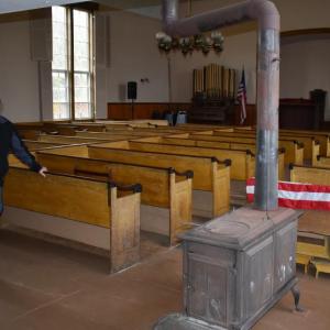 Selectman Allen Greene inside Woolwich’s Nequasset Meeting House. At right is one of three woodstoves once used to heat the building. Beneath the pew are footstools. PHIL DI VECE/Wiscasset Newspaper