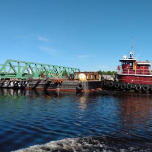 Winslow Marine uses a tugboat to help the barge carrying the last piece of Barters Island Bridge maneuver down the Kennebec River. Mark Stover photo