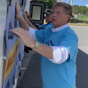 Maine Sen. Bill Diamond, D – Windham, foreground, and Rep. Jeff Hanley, R – Pittston, put a poster on a camper at Wiscasset Community Center Wednesday afternoon, Sept. 29, for a stop on Diamond’s “Walk a mile in their shoes tour” promoting child protective services reform and honoring Wiscasset’s Kendall Chick and other slain children. SUSAN JOHNS/Wiscasset Newspaper