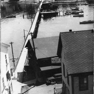 It’s difficult to get a good view of the footbridge. This one from the 1940s or 1950s looks to the east side of Boothbay Harbor. In the foreground is the north end of the Romar bowling alley. Halfway across the footbridge is the bridge house near the dock and float extending south. The house is obscured by being so dark. Courtesy of BRHS