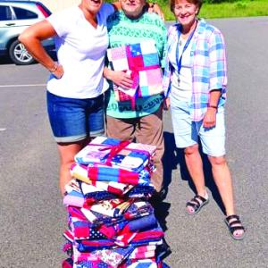 Erin Barter, left, veteran Ernie Gagnon and Cabin in the Woods Community Coordinator Auta Main stand by the 21 quilts ready to be distributed to veterans. Courtesy VOA Northern New England